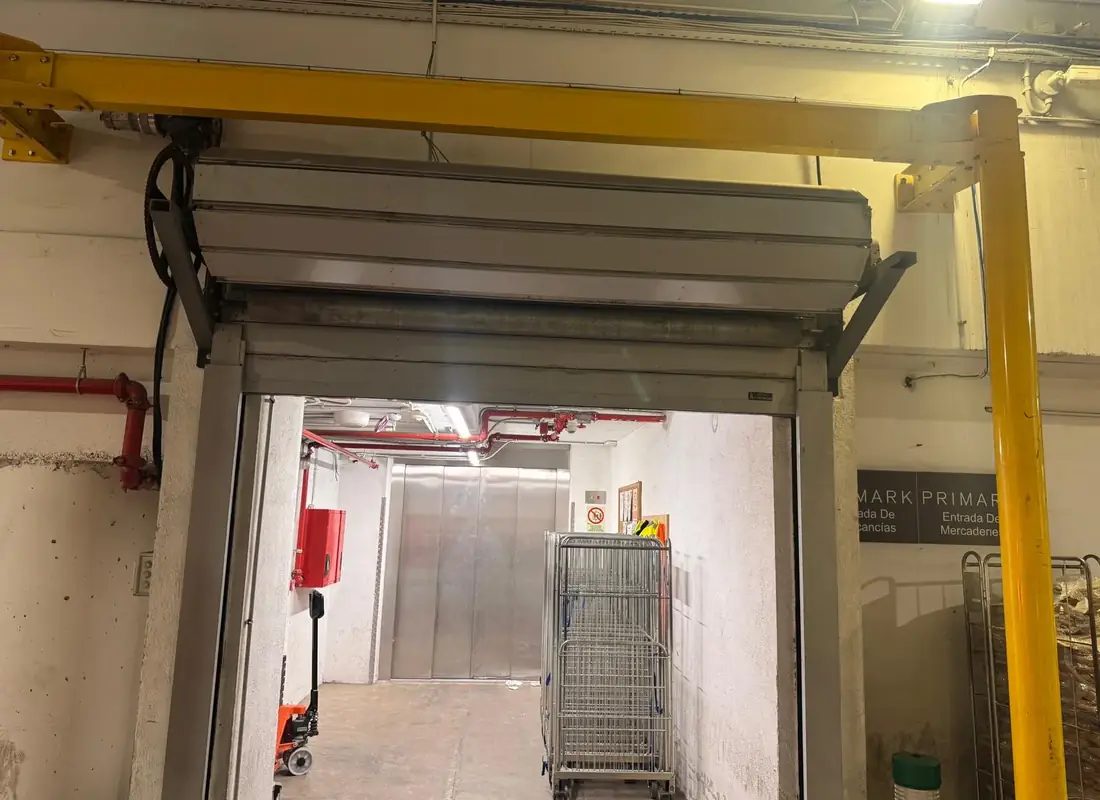 Puerta enrollable metálica en el acceso de mercancías de un almacén comercial, con carros de reparto al fondo